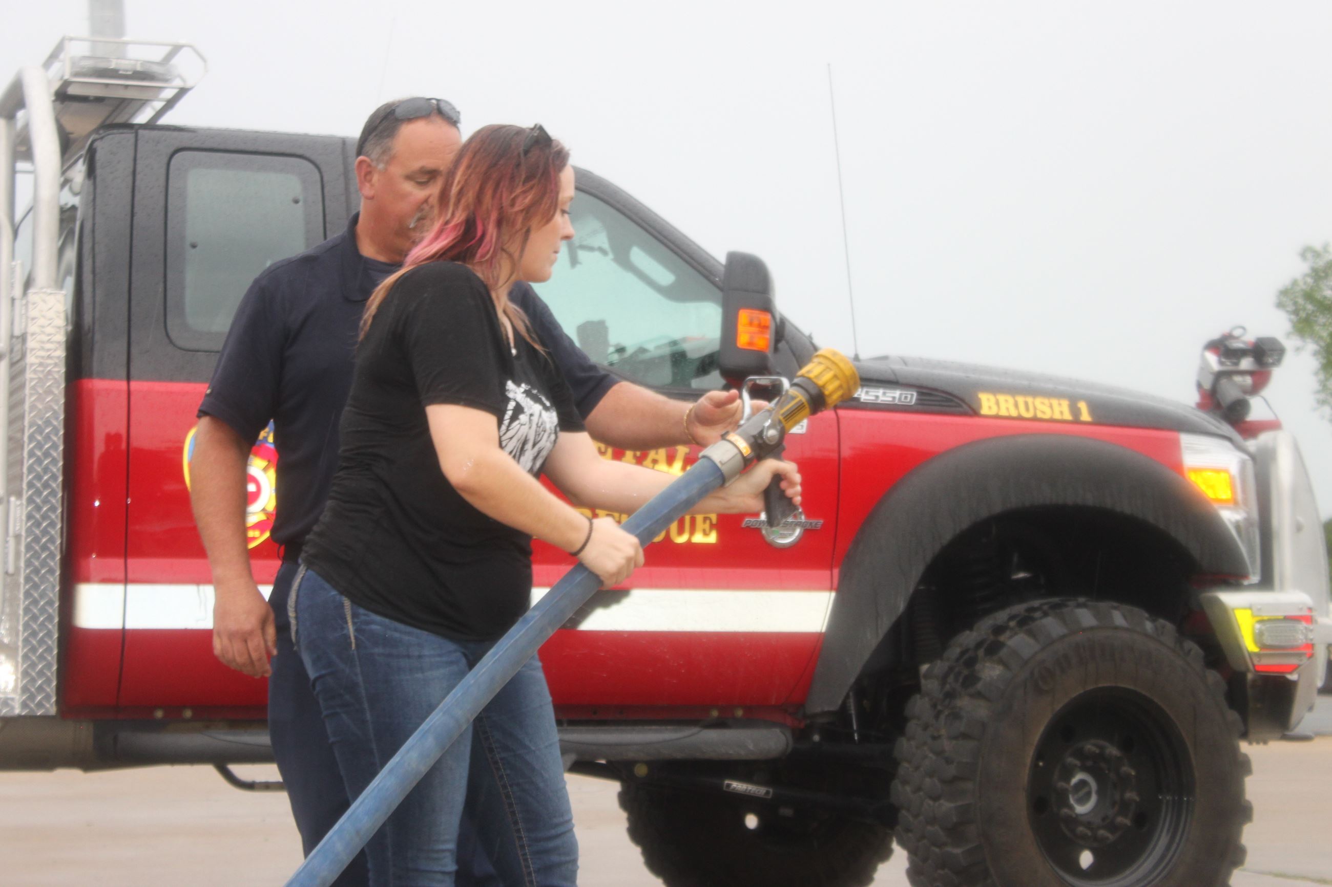 A firefighter teaches someone how to use a fire hose