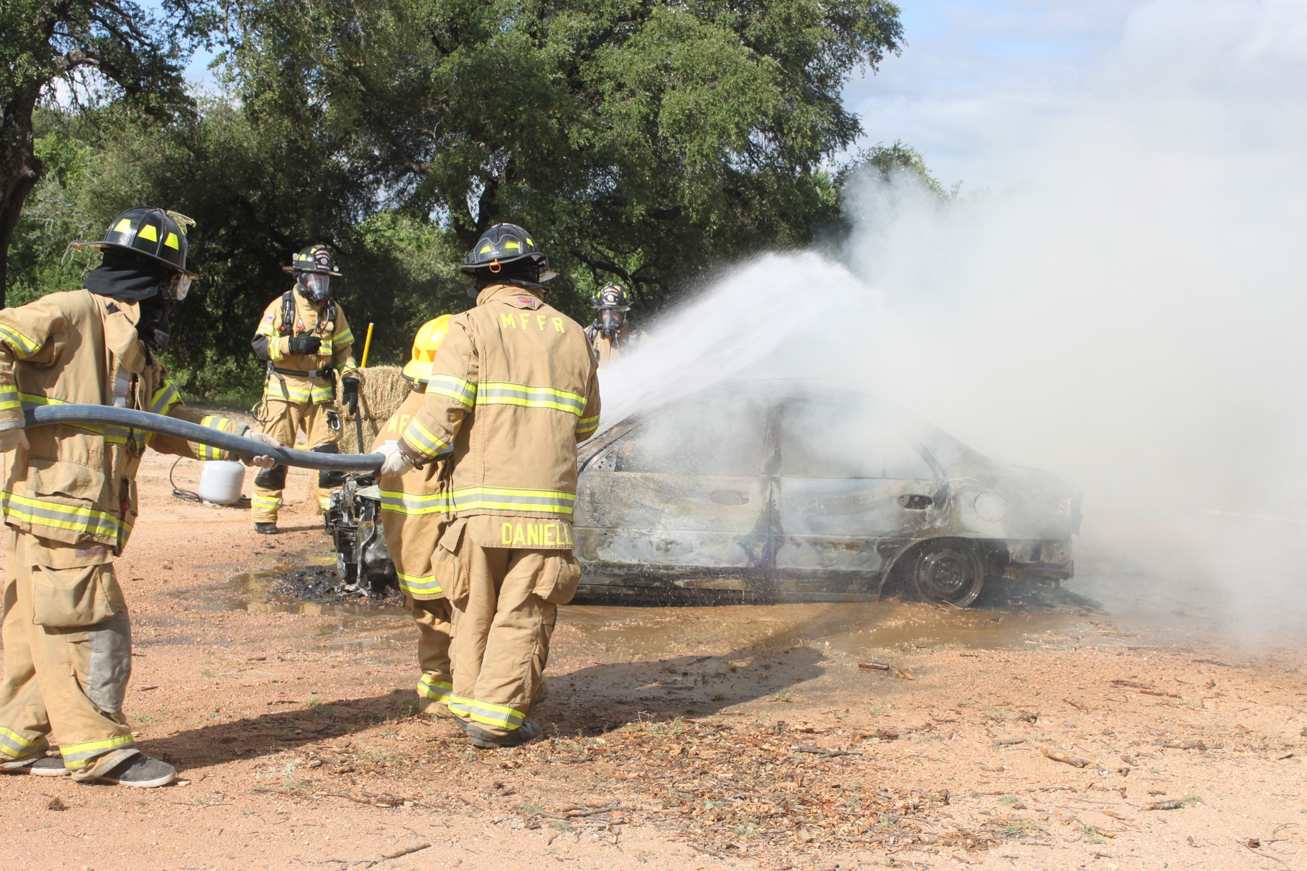 Firefighters use hoses on a burning car