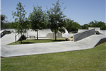 Photo of grassy area with trees in the center of the skate park.